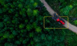 Aerial view of an industrial vehicle operating through a forested area, representing practical sustainability in industrial operations.